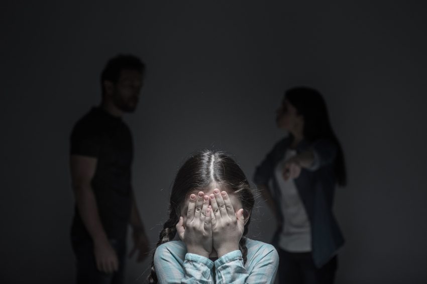 upset young girl with parents fighting in background - trauma