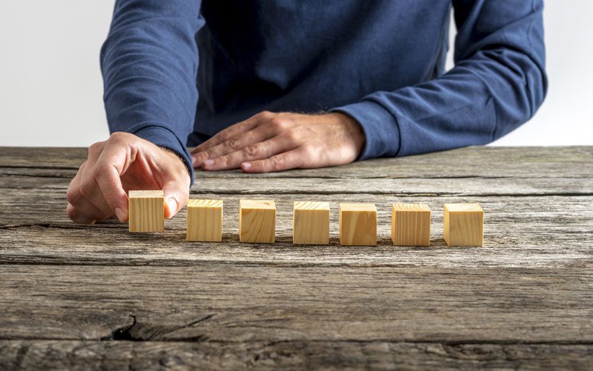 man setting up 7 wooden blocks on a table - loved ones