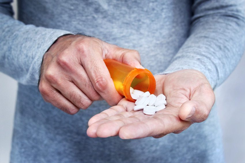 person pouring out white pills from bottle into hand - opioid addiction